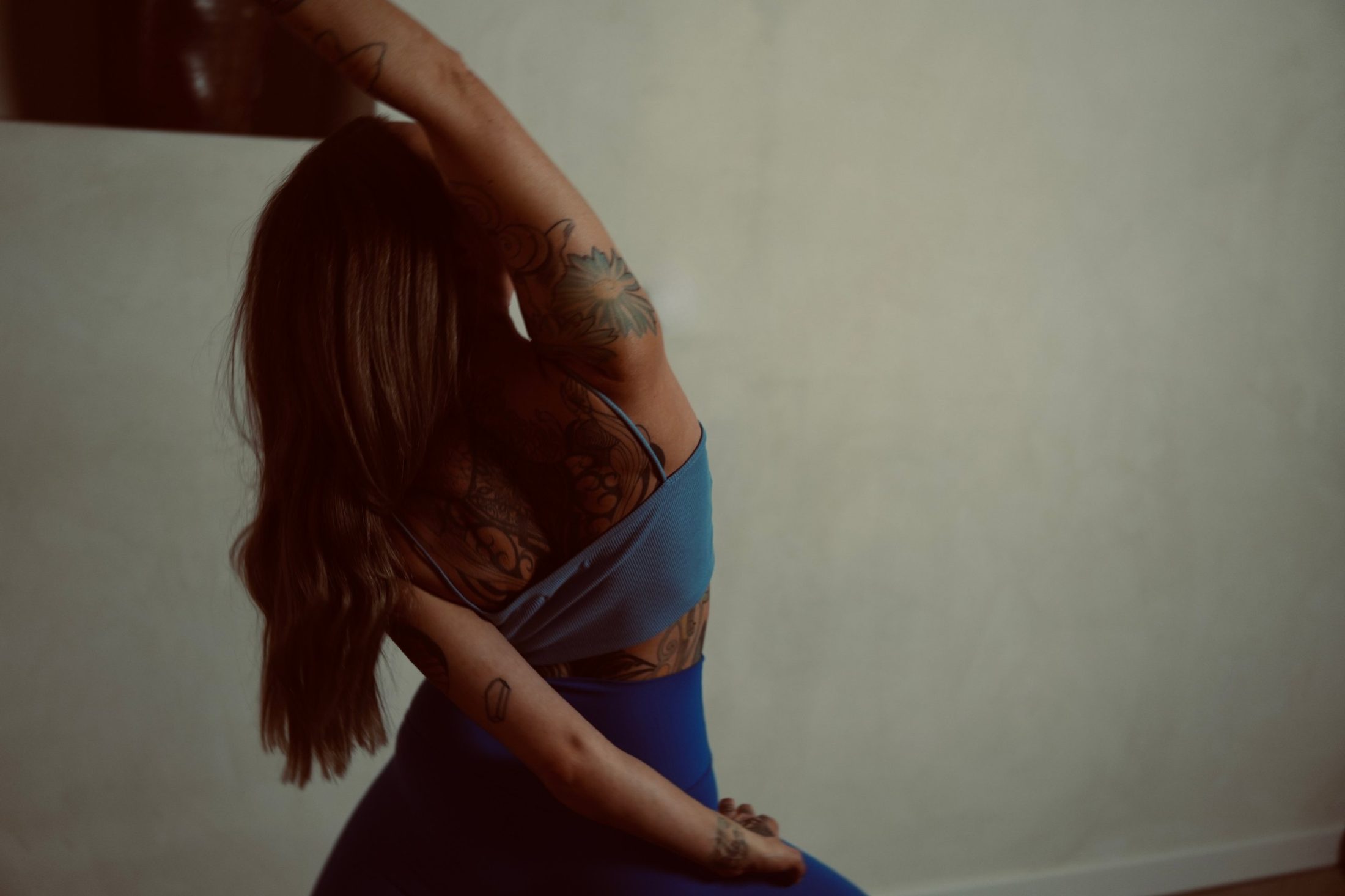 Chiara in einer sanften Seitdehnung, ein Arm über dem Kopf, vor einer hellen Wand